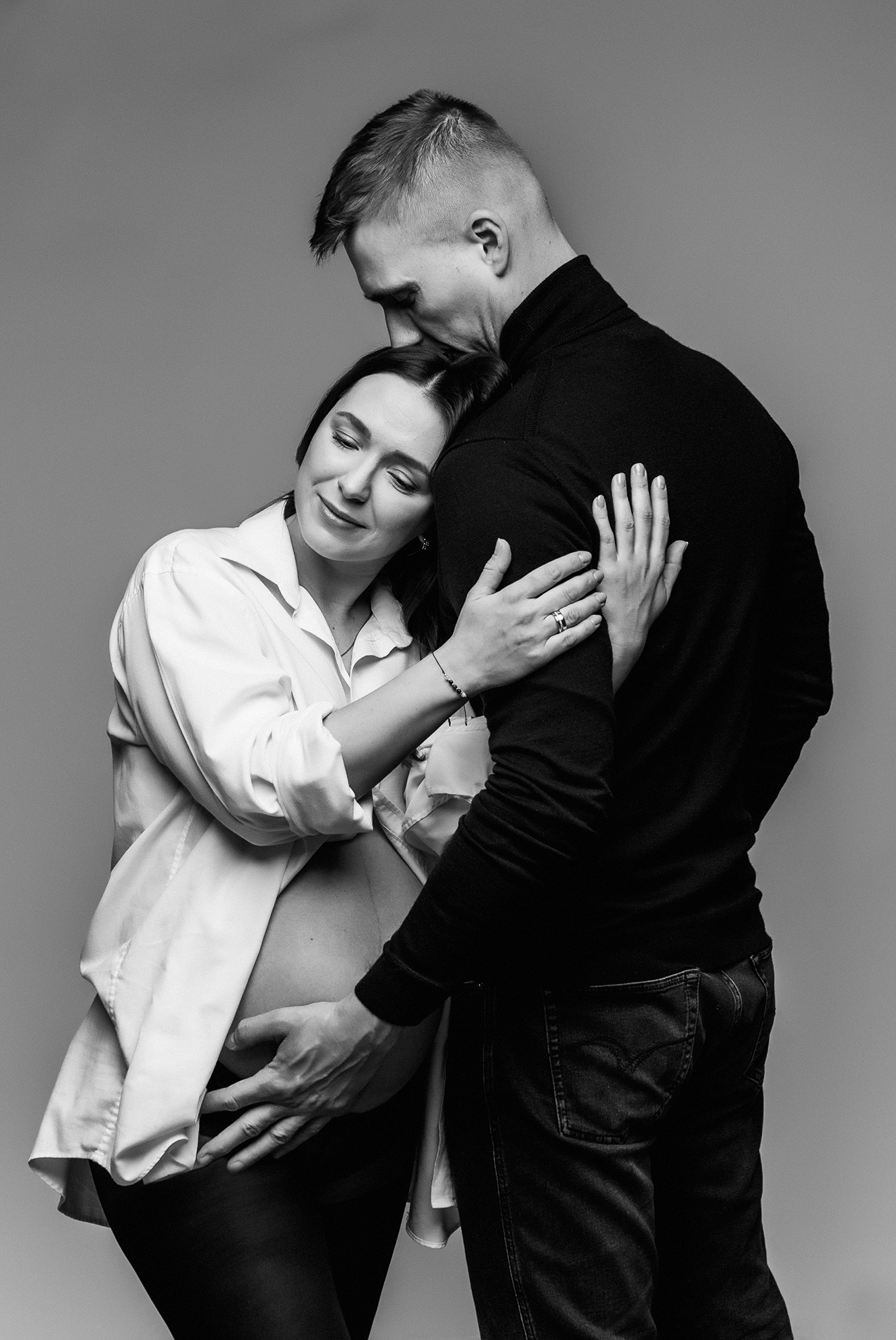 Sesja brzuszkowa z partnerem w studio; małżeństwo na czarno-białym ujęciu, kobieta w rozpiętej męskiej koszuli fotograf Warszawice Studio-S fotografia rodzinna